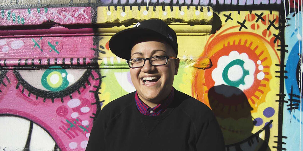 Photo of Gabby Rivera laughing in front of a public mural