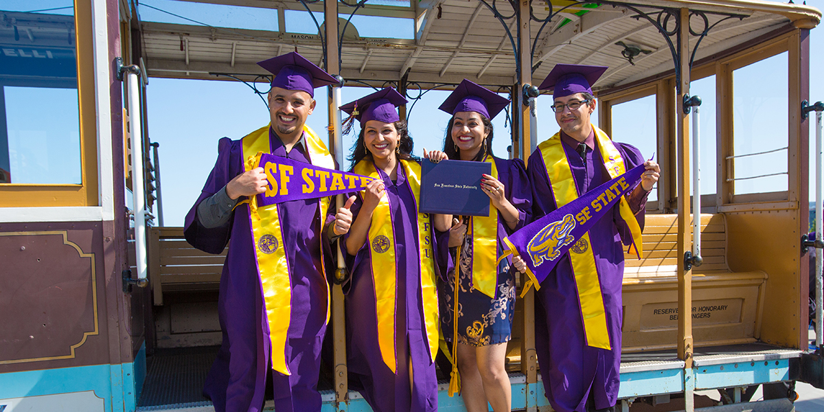 Photo of four students holding SF State pennants and diplomas at Commencement