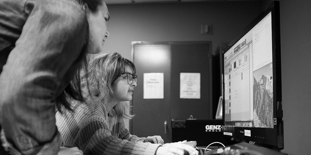 Photo of two students using a desktop computer to edit film