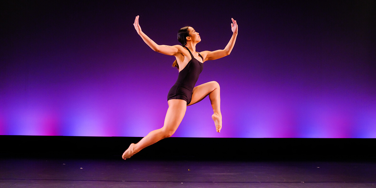 Photo of student dancer Francez Urmatan leaping in front of purple stage lighting