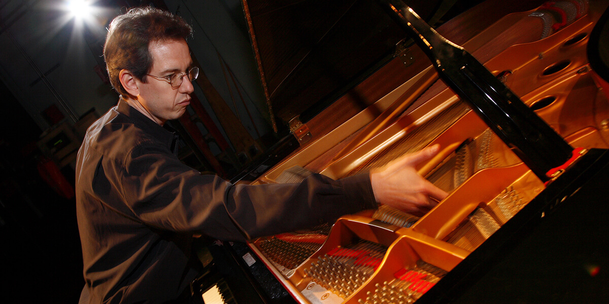 Photo of Christopher Adler playing the treble bridge part under the lid of a piano