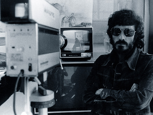Photo of Franco Beltrametti with his arms folded near film camera and monitor