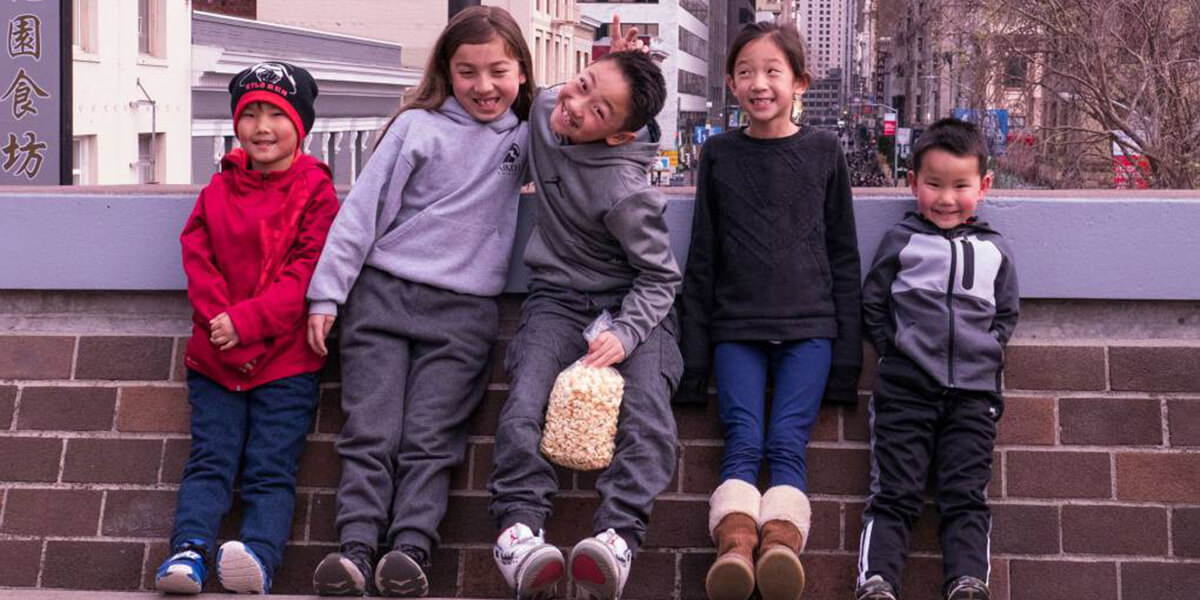 Five children smile while posing for a picture in front of a short brick wall on the bridge at Portsmouth Square in San Francisco's Chinatown