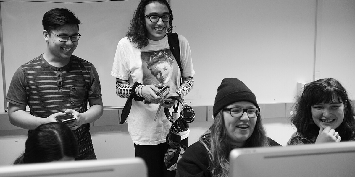 Black and white photo of four students laughing in a computer lab