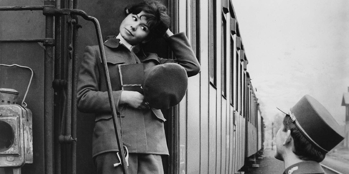 Black and white photo of man and woman talking outside of a train