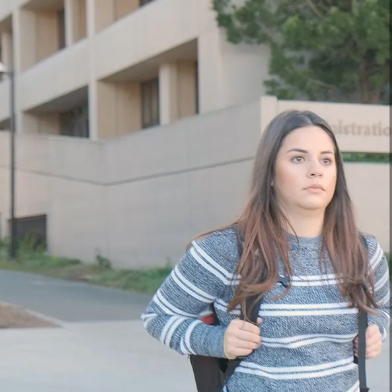 Photo of Mikayla Cordero walking past the Administration Building wearing a backpack