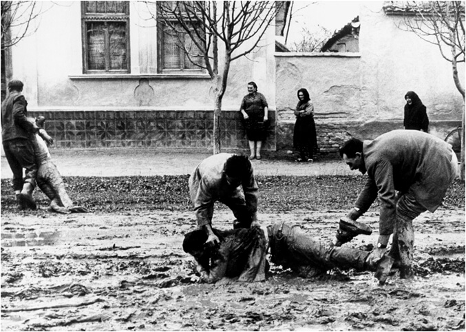 Black and white photo of two men helping pick up a man off of the ground