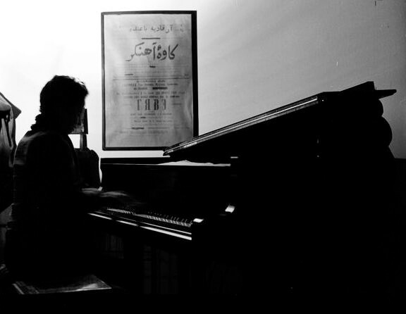 Black and white photo of person playing piano in front of poster with Persian type
