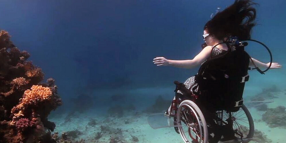 Photo of woman in wheelchair underwater near a coral reef