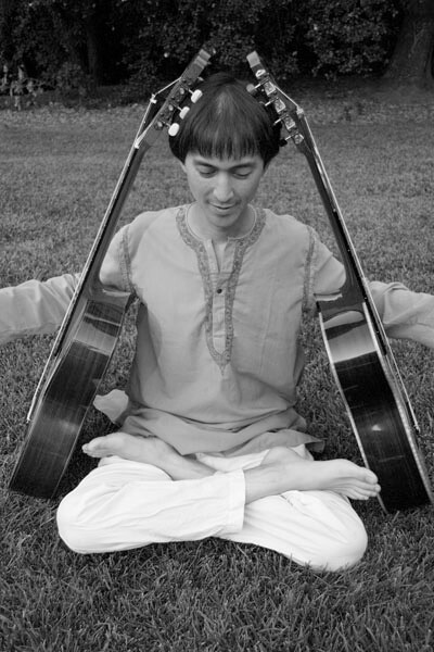 Black and white photo of Matthew Grasso in a yoga pose with two acoustic guitars leaning against his body