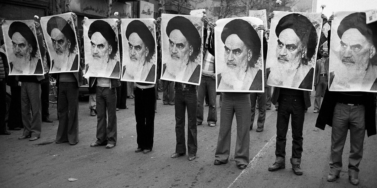 Black and white photo of row of men holding photos of Ruhollah Khomeini