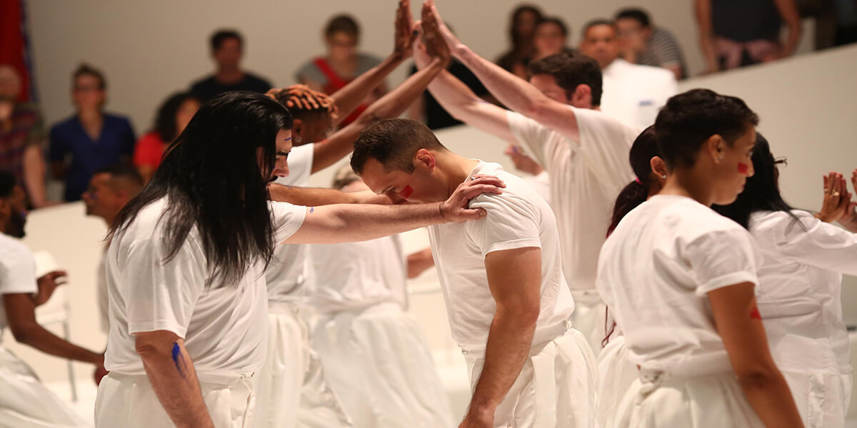People dressed in white holding up their arms above a man bowing down