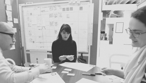 Black and white photo of George Aye, Elaine Lopez and Annemarie Spitz working with paper at a design studio