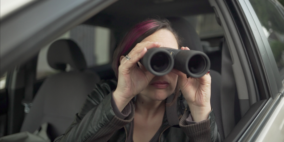Photo of Jessamyn Lovell using binoculars while sitting in a car