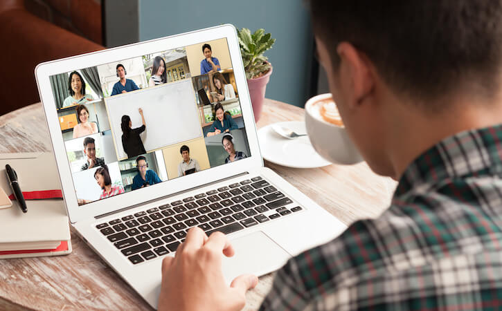 Photo of man participating in Zoom meeting while seated at desk and typing on a laptop computer