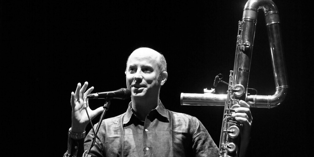 Black and white photo of Ned McGowan standing in front of microphone holding contrabass flute