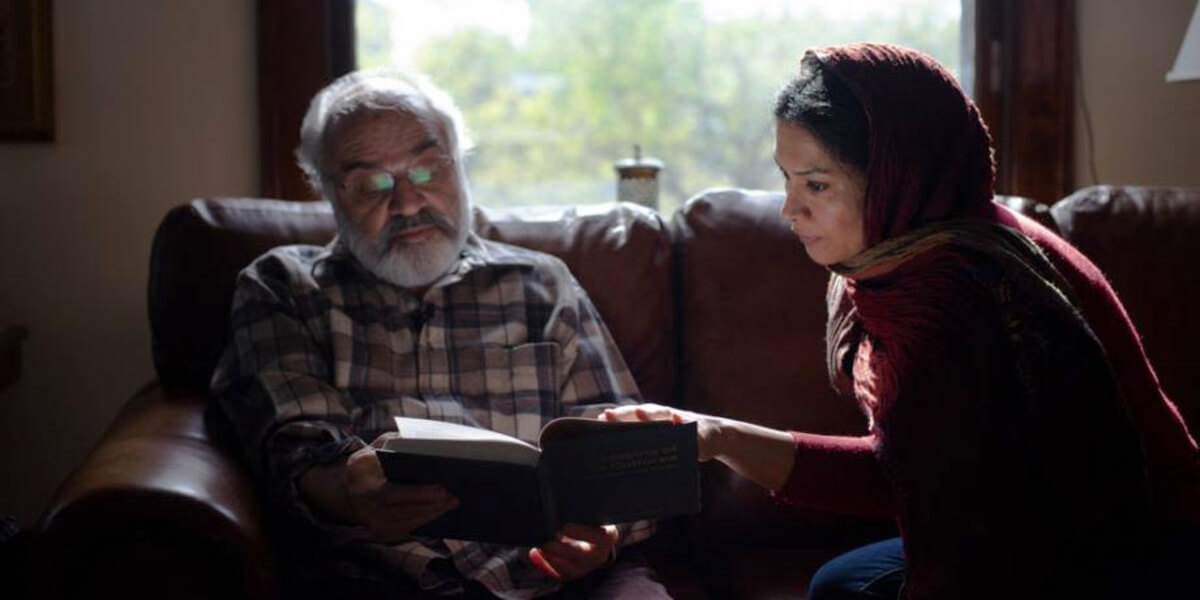 Photo of Hamid Naficy and a woman reading a book together while sitting on a couch