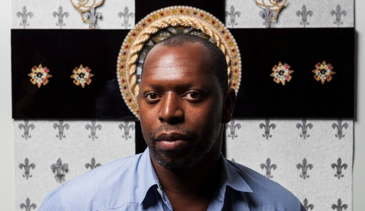 Photo of Rashaad News standing in front of a cross and fleur-de-lis wallpaper