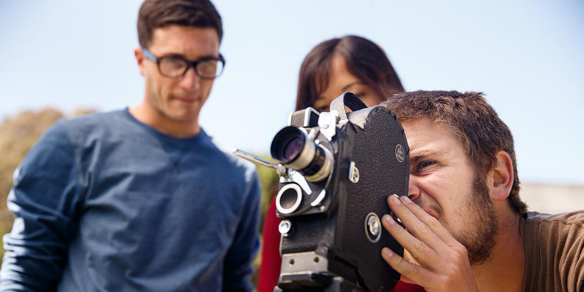 Photo of student shooting film while two students in background look over his shoulder