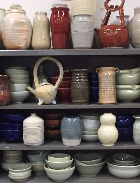 Photo of shelves filled with ceramic plates, kettles, planters