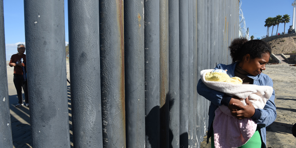 Photo of woman holding baby next to fence on U.S.-Mexico border