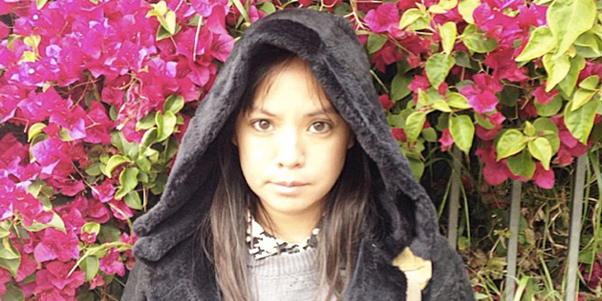 Photo of Feliz Lucia Molina wearing a hood in front of flowers and bushes