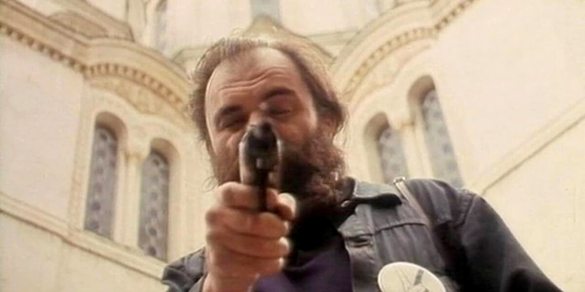 Photo of bearded man pointing a gun at the camera