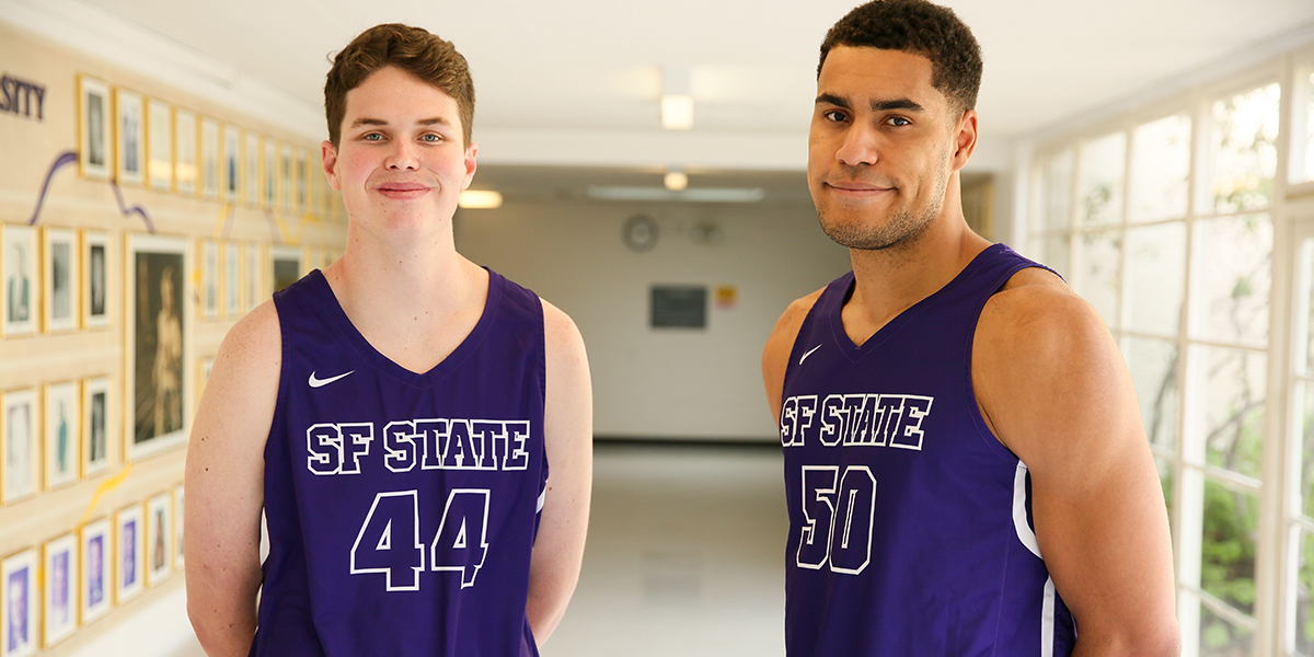 Photo of Ryne Williams and Tyler Jackson wearing purple practice uniforms in Gymnasium hallway