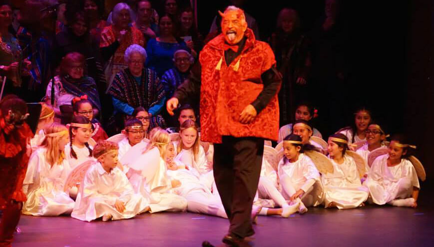 Photo of Carlos Baron in performance dressed as a devil in front of children dressed as angels