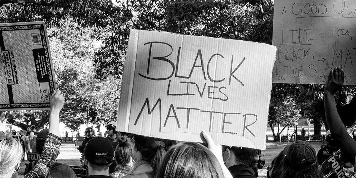 Black and white photo of a woman holding a Black Lives Matter cardboard sign at a protest at the White House
