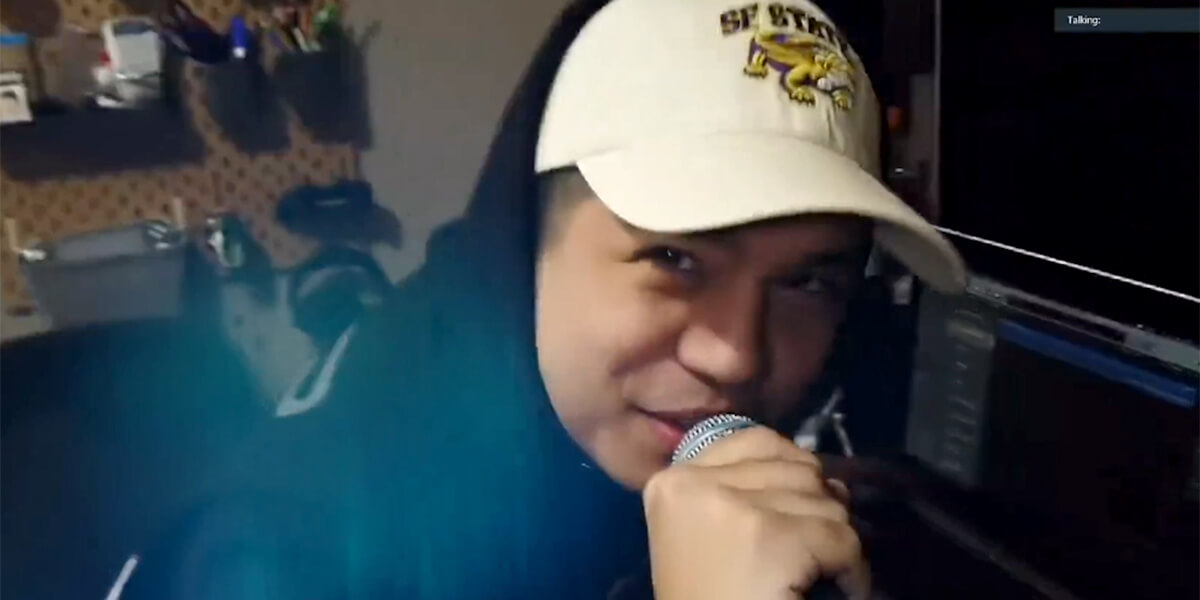 Daric Carvajal rapping while holding a microphone in his home while wearing a white SF State Gators baseball cap