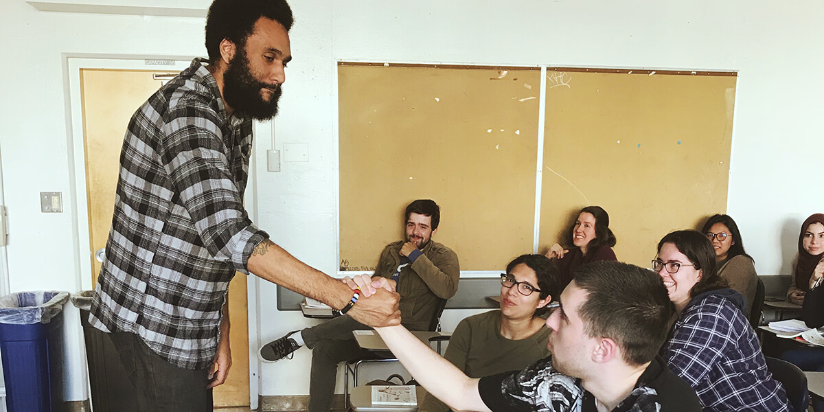 Photo of Tongo Eisen-Martin shaking hands with a student during a classroom talk