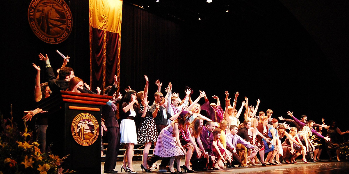 Drama students throw their hands in the air on stage