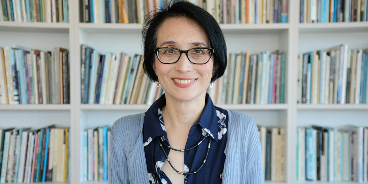 Photo of May-lee Chai standing in front of bookshelves at The Poetry Center