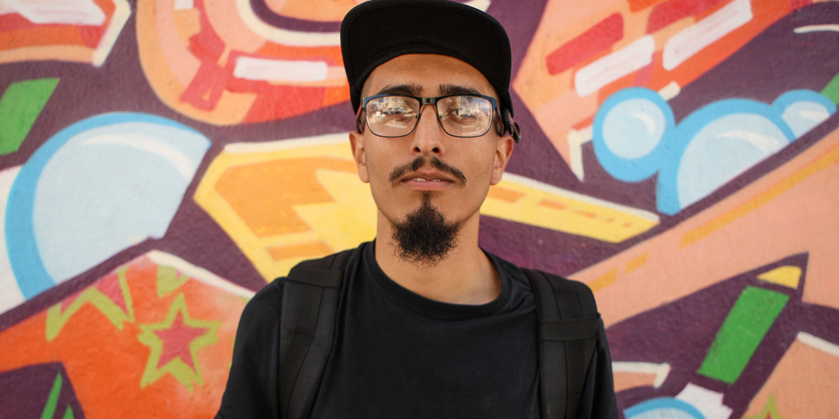 Photo of Joel Angel Juarez in front of a graffiti mural