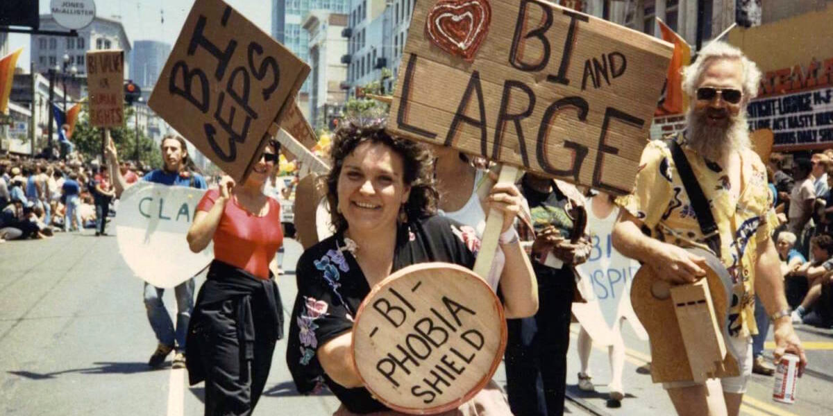 Photo of Lani Ka’ahumanu marching in Pride Parade holding shield reading "Bi-Phobia"