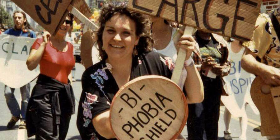 Photo of Lani Ka’ahumanu marching in Pride Parade holding shield reading "Bi-Phobia"