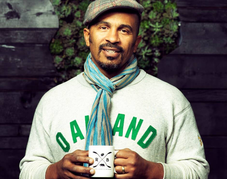 Photo of Keba Konte holding a cup of coffee and wearing an Oakland sweater