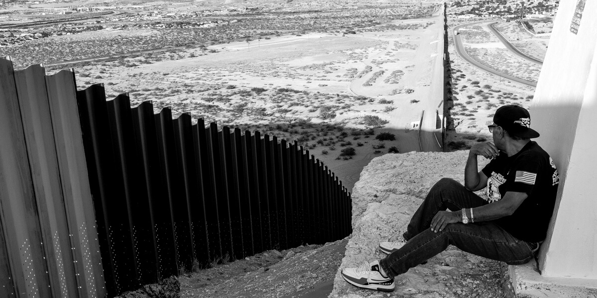 Black and white photo of Jose Francisco Lopez Moreno overlooking fence at U.S.-Mexico border