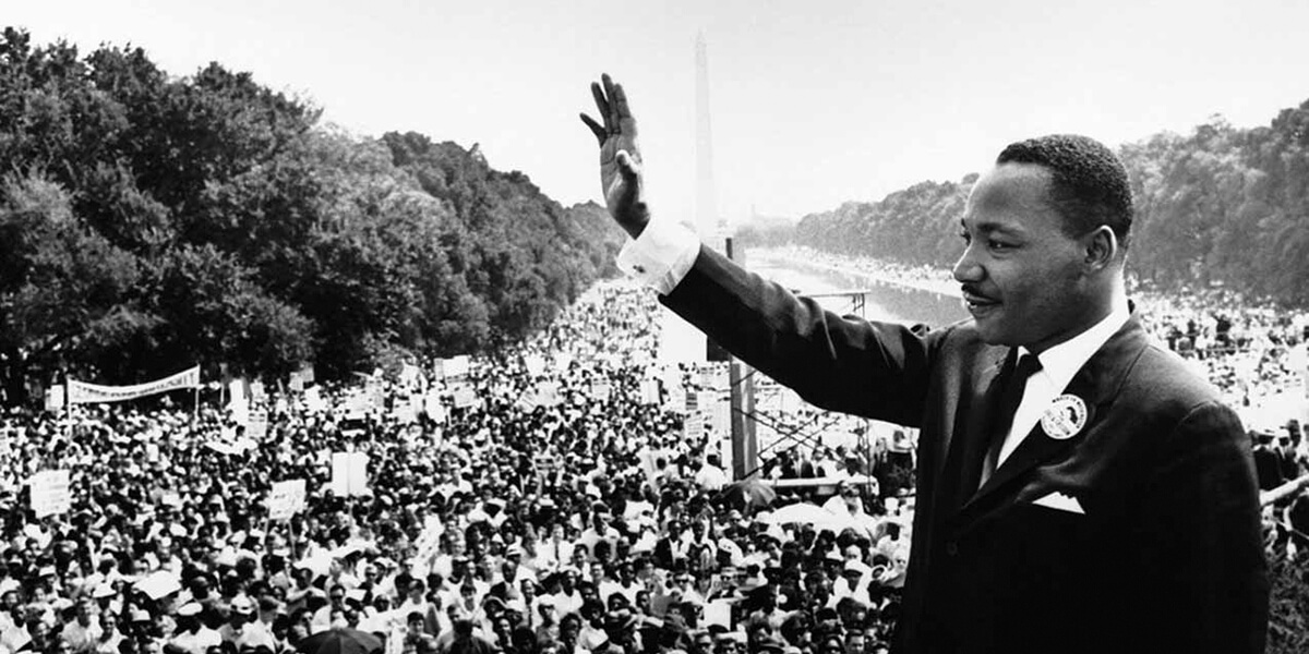 Black and white photo of Martin Luther King Jr. waving in front of large crowd