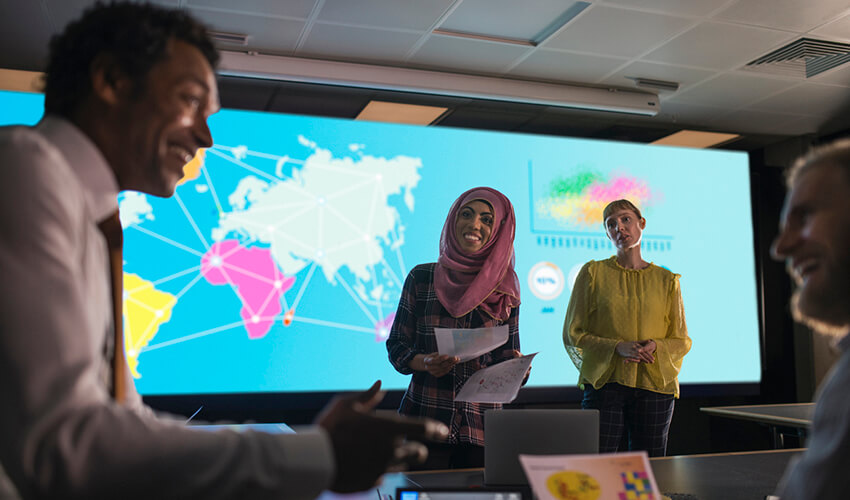 Photo of students delivering a presentation in front of screen showing world map