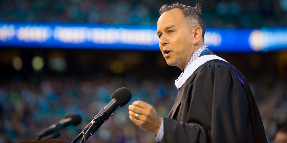 Photo of Jonas Rivera wearing graduation gown and speaking at SF State Commencement