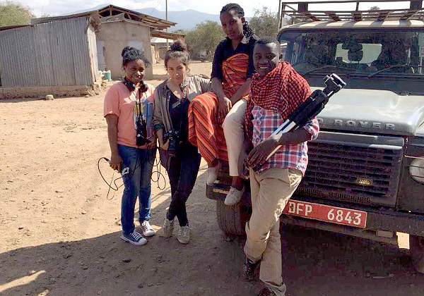 Photo of Adreanna Rodriguez and Tanzanian youth with camera equipment standing by a jeep