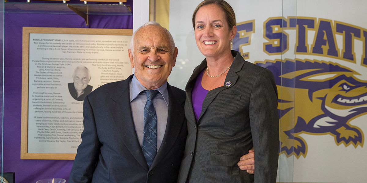Photo of Ronnie Schell and Stephanie Shrieve-Hawkins in front of Schell plaque and SF State logo