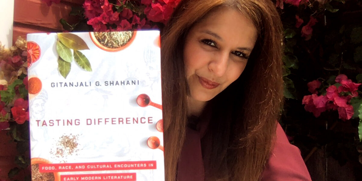 Photo of Gitanjali G. Shahani in a garden holding her book Tasting Difference: Food, Race and Cultural Encounters in Early Modern Literature