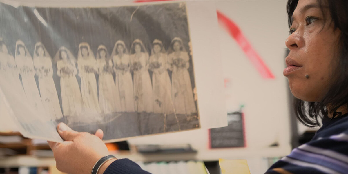 Celine Parreñas Shimizu holding up an archival black and white photo of a bride and nine bridesmaids