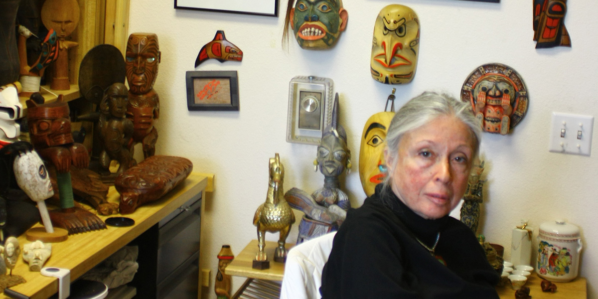 Photo of Anita Silvers seated near tribal masks