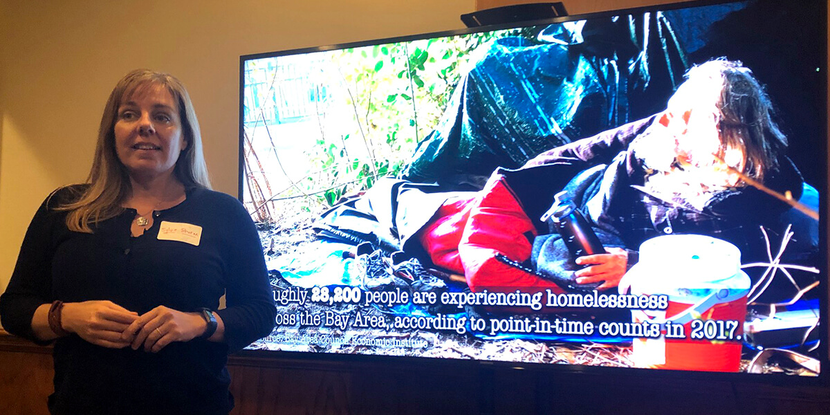 Photo of Sylvie Sturm standing in front of screen showing unhoused man next to a tent