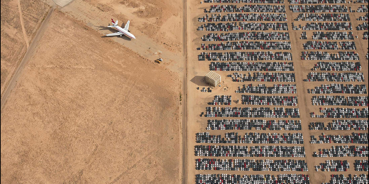 Aerial photo of hundreds of Volkswagens and one airplane parked in rural area