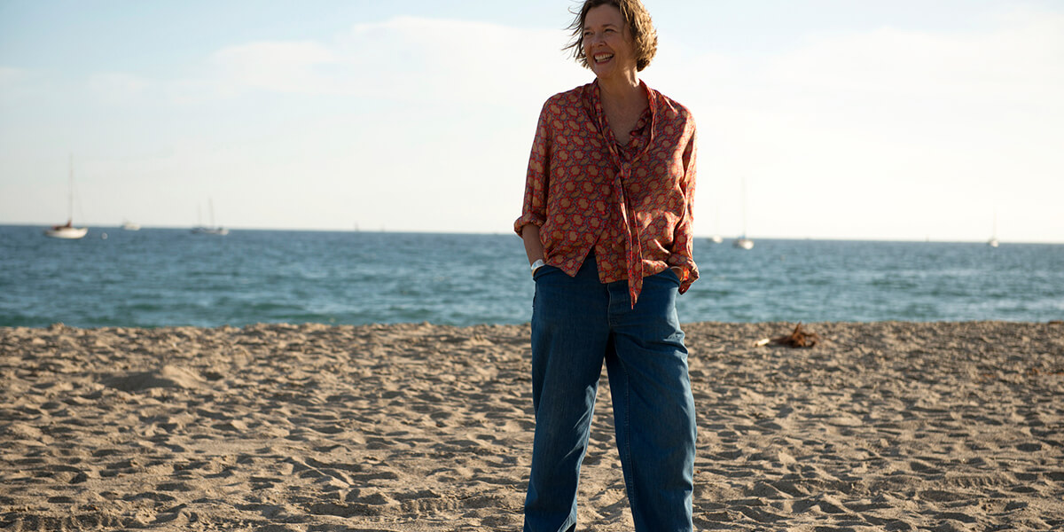 Annette Bening standing and smiling on a beach